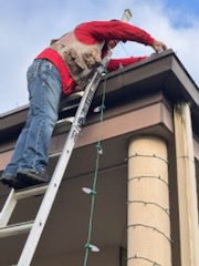 Installer at the top of a ladder securing lights at the gutter line